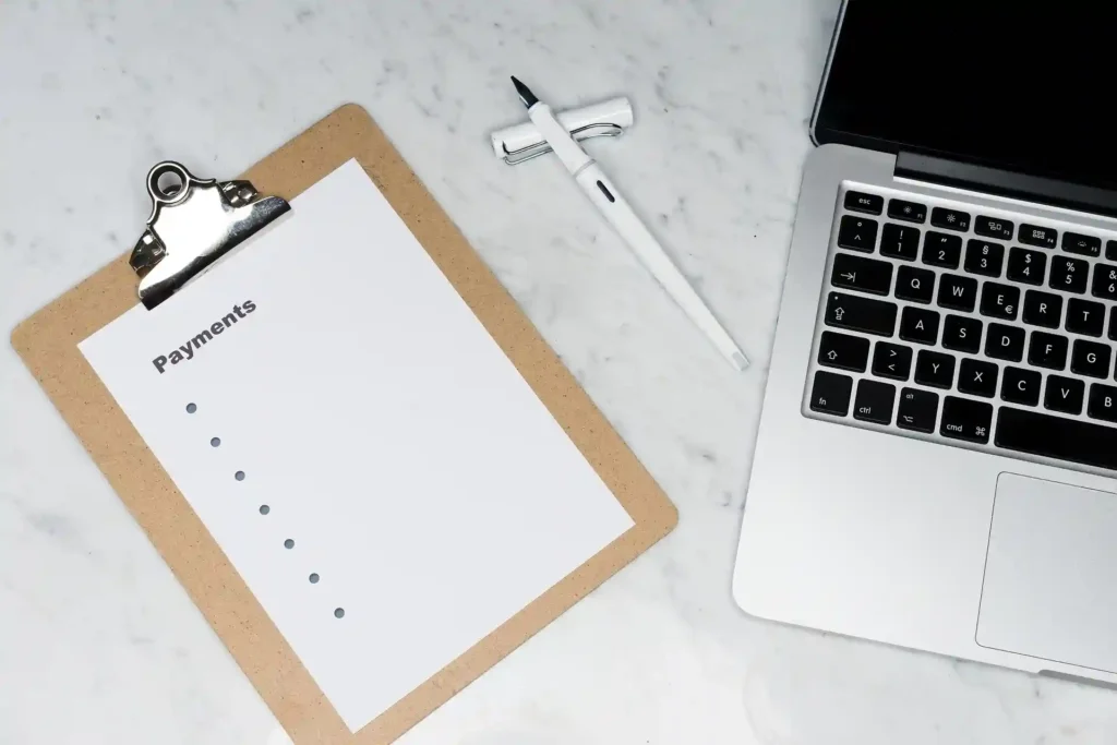 Clipboard with a payment checklist next to a pen and laptop, representing the procurement and building tender process in construction projects.