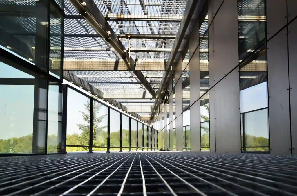 Modern architectural space with large glass panels and metal grid flooring, highlighting advanced building management systems for efficient design and maintenance.