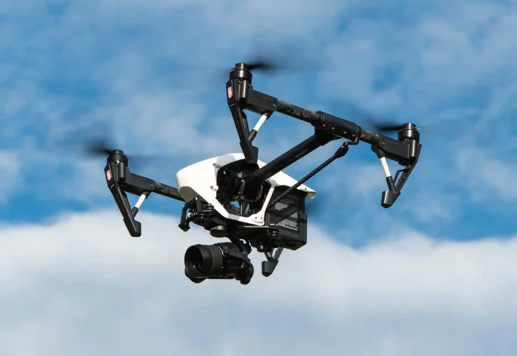 High-tech drone equipped with a camera flying in a blue sky, used for construction site monitoring and aerial inspections.