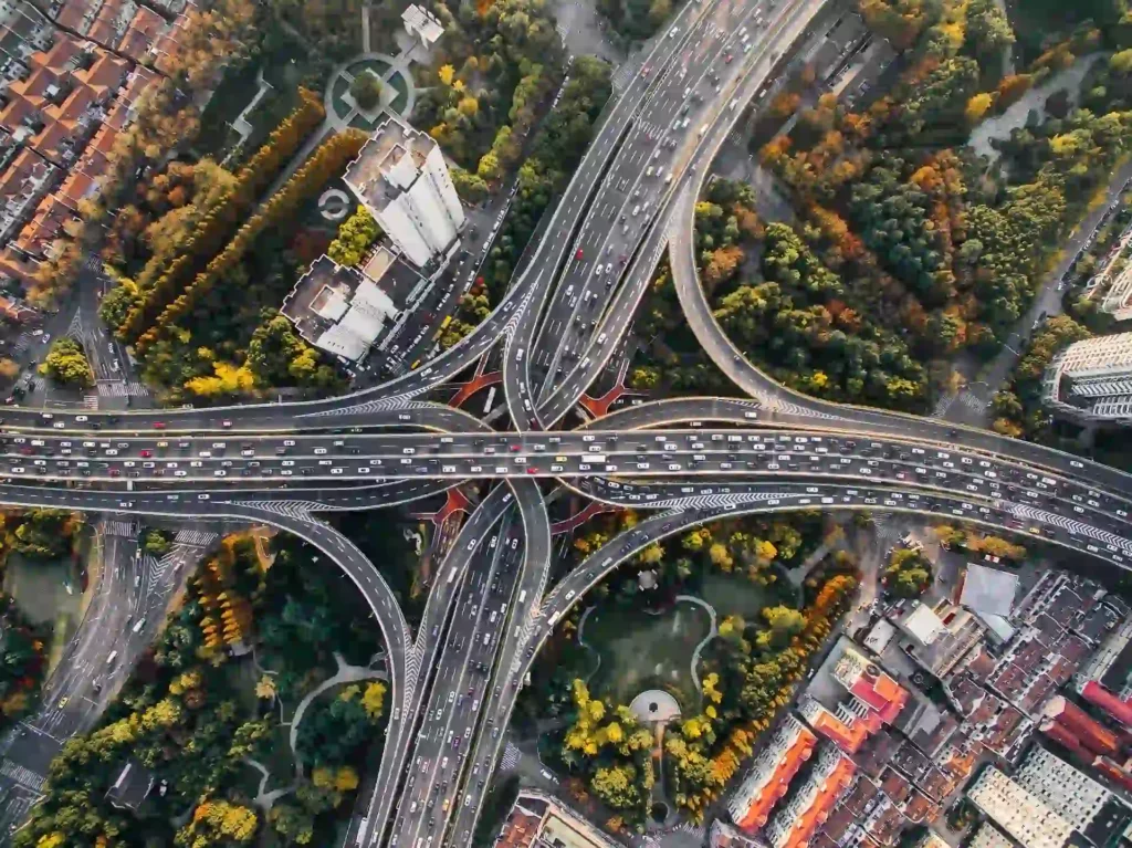 Aerial view of a complex highway interchange surrounded by urban and green spaces, illustrating infrastructure design and urban planning